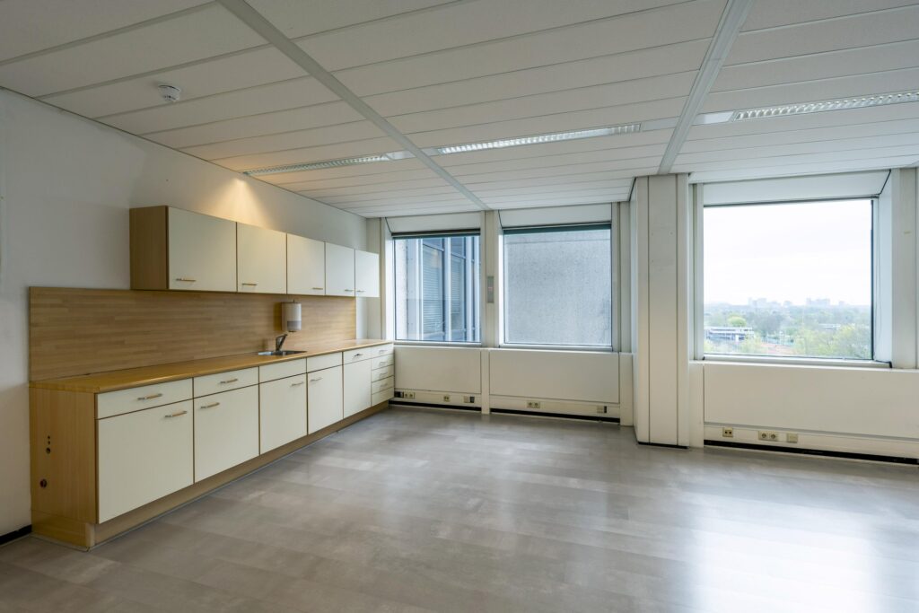 Modern kitchenette with light cabinets and large windows in an office space on Laan van Kronenburg.